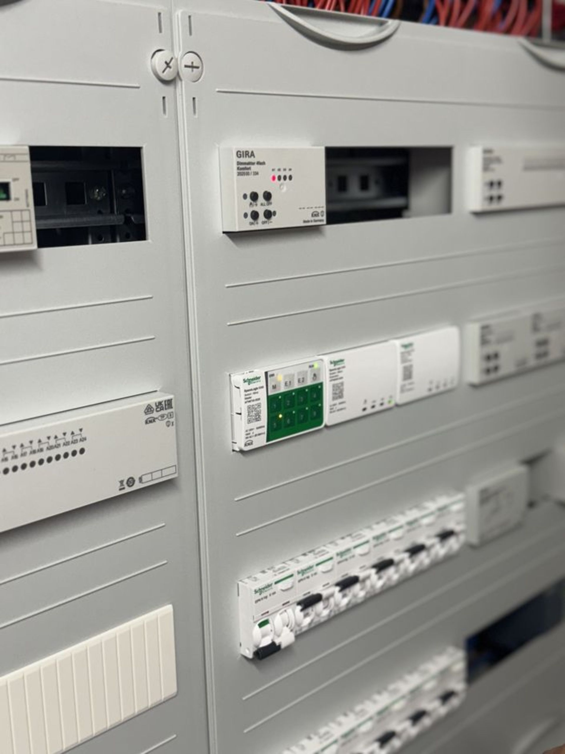 Graue Wand mit mehreren elektrischen Schaltkästen und Steuergeräten. Sichtbare Marken sind GIRA und andere, mit verschiedenen Tasten und Anzeigen.