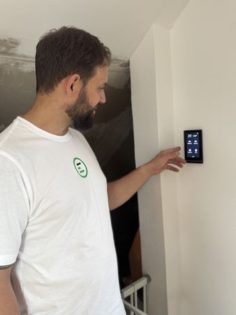 Mann in weißem T-Shirt bedient ein schwarzes Wandgerät mit beleuchtetem Display