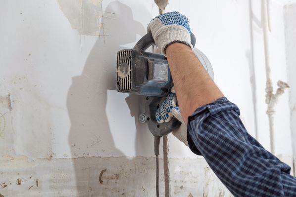 Handwerker mit Arbeitshandschuhen fräst mit einer Mauerschlitzfräse einen Kabelschlitz in die Wand.